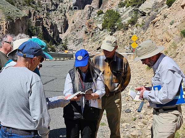 Geology field trip participants consult a fossil book with Larry Oliveria.