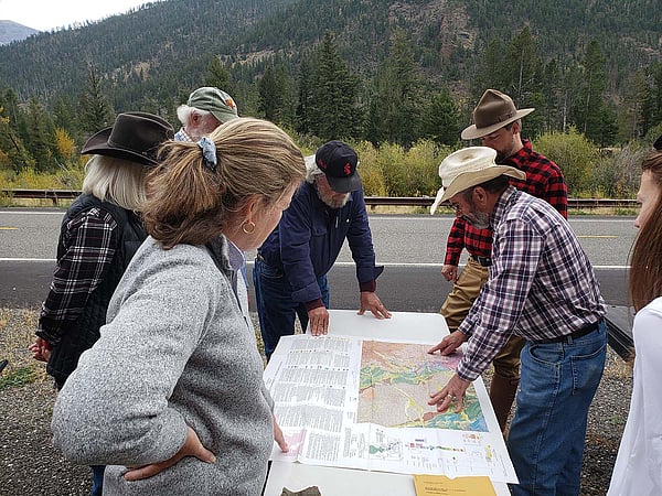 Geology field trip participants gather around as an instructor reads a map.