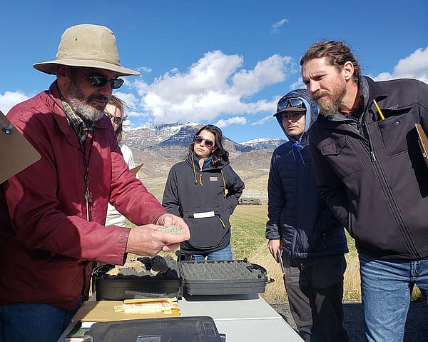Larry Oliveria shows different types of rock as geology field trip participants gather around.