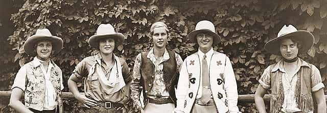 Five women dressed in western clothing in front of a hedge.