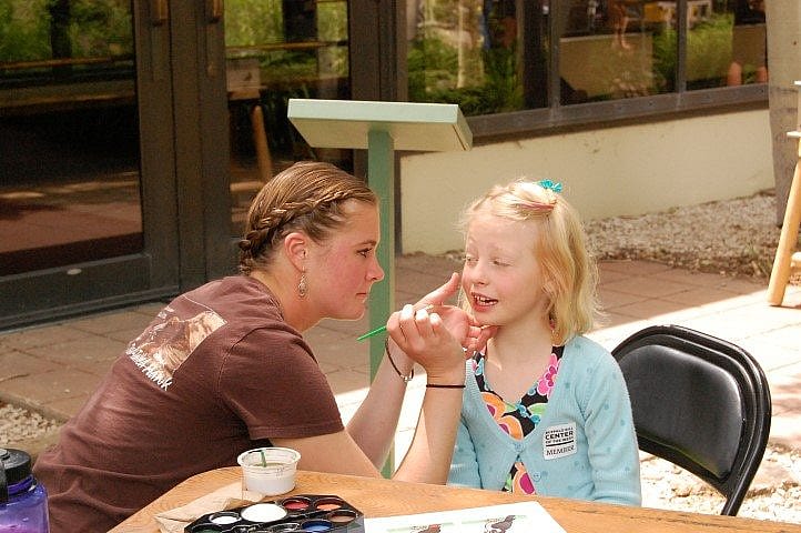 Woman painting a peregrine falcon on a child's face.