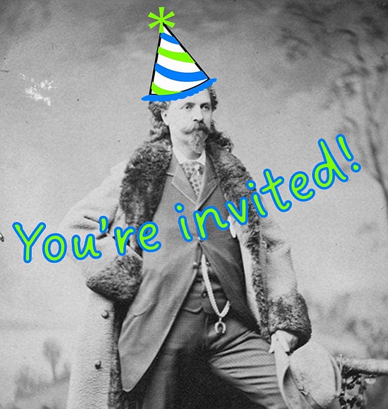A portrait of Buffalo Bill standing in front of a painted backdrop. He wears a full length fur trimmed coat, a three piece suit and a gold chain with horseshoe pendant. He has one leg up on a block and holds his hat over his knee. P.6.0124