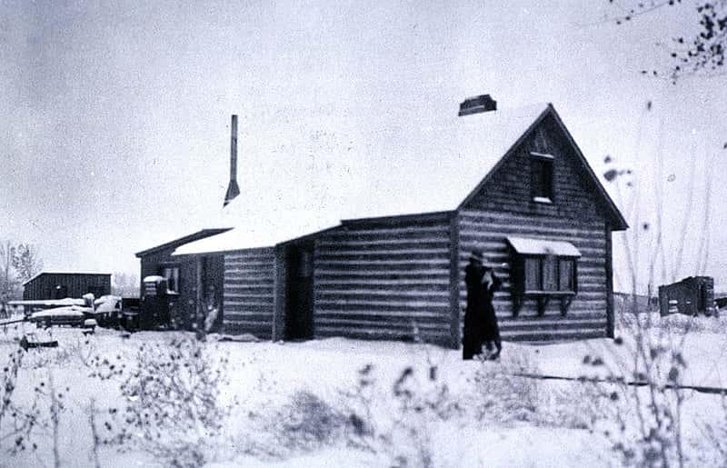 Absarokee Hut in winter, ca. 1905. Addie Sharp stands on the front walk, holding her dog Frans Hals. P. 22.523
