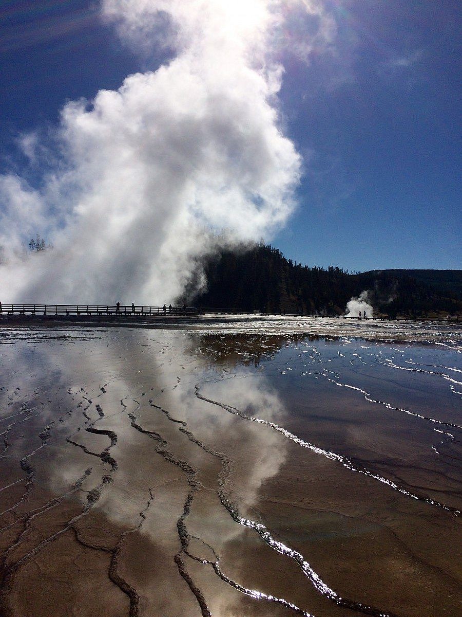 Steam rising from Grand Prismatic Spring in Yellowstone National Park, with reflections on the thermal runoff and a boardwalk in the distance.