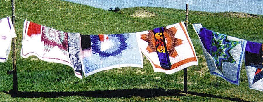 Blowing quilts at a memorial giveaway for Max Mesteth, brother of Freda Goodsell, Manderson, South Dakota. Quilts by Freda Goodsell. August 24, 2000. Photo by Arthur Amiotte.