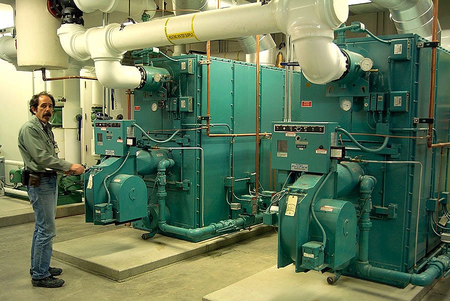 Operating Engineer Phil Anthony is pictured with boilers that will take on the load of heating older parts of the Center, areas where inefficient and outdated equipment will be scrapped.