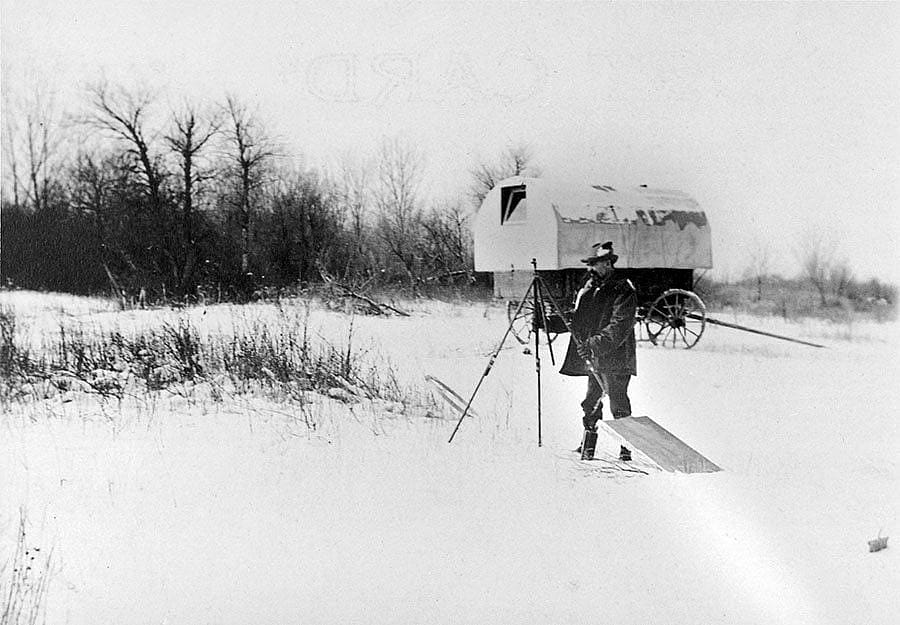 "Setting up, 'Prairie Dog' in background, Crow Agency, Mont. ca. 1900." Artist Joseph Henry Sharp was also a photographer. This print shows him setting up his easel in the snow, with his covered wagon studio that he nicknamed "Prairie Dog" behind him. P.22.42