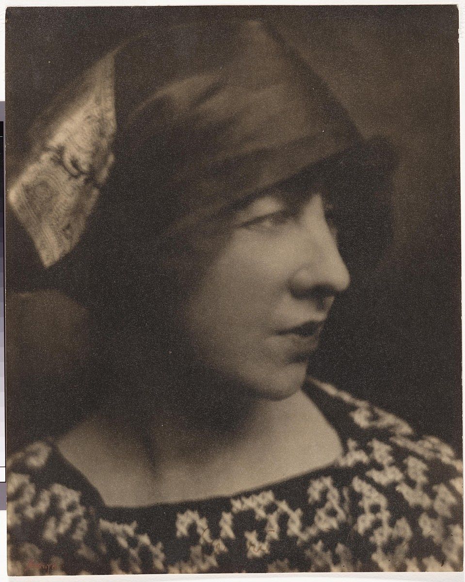 Vintage portrait of Gertrude Vanderbilt Whitney wearing a patterned dress and a stylish hat, in a sepia tone.