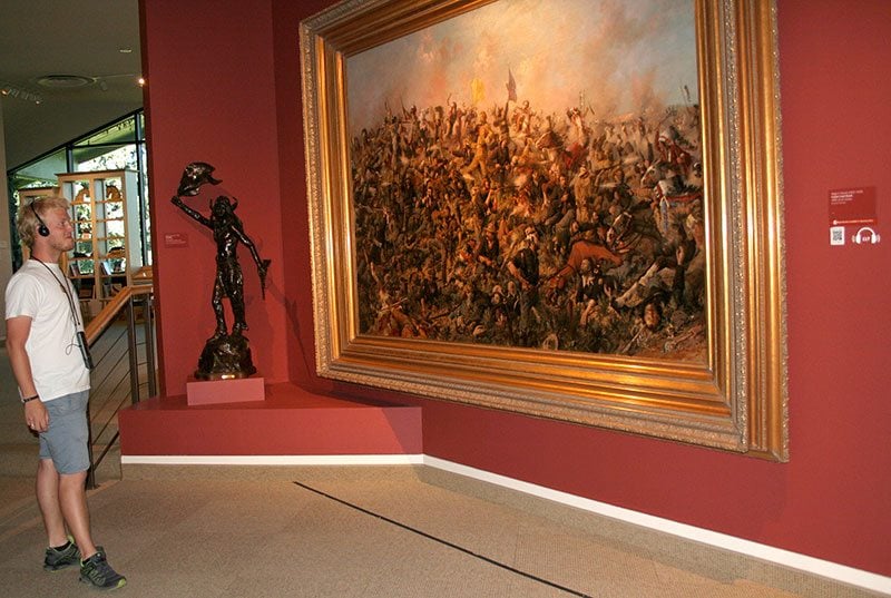 A summer visitor to the Whitney enjoys an art expert's perspective by using a new, free audio guide. The painting is Edgar S. Paxson's "Custer's Last Stand," 1899. Museum Purchase. 19.69