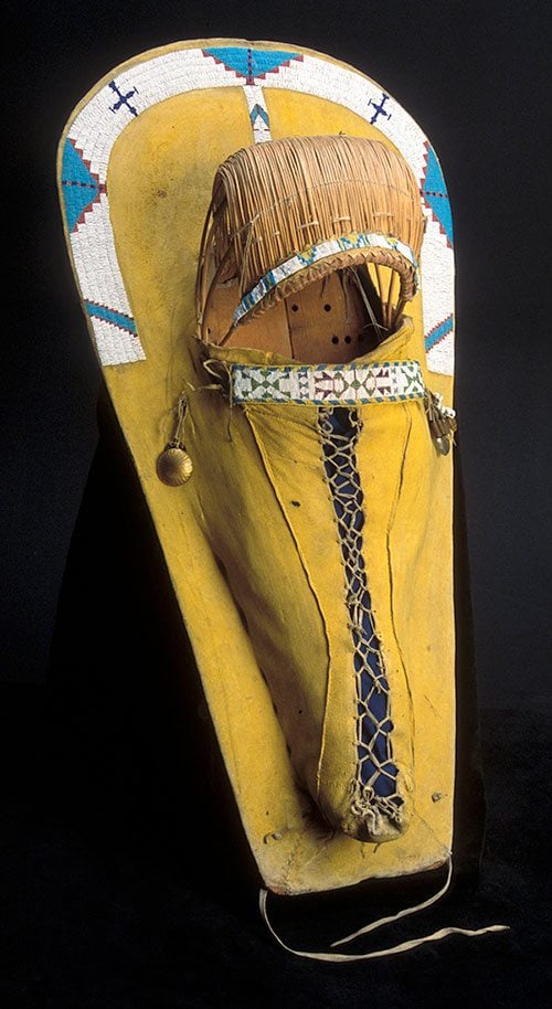 Cradle, late 1800s. Ute, Southern Colorado or Utah. Tanned deer hide, wood, willow, glass beads, pigments, brass, cowrie shells. Gift of Corliss C. and Audrienne H. Moseley. NA.111.19