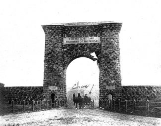 Frank J. Haynes photograph of Roosevelt Arch. Charles Ackelmire identified as man in wagon. MS 21 Yellowstone National Park Collection, McCracken Research Library, Buffalo Bill Center of the West. 21.217.12