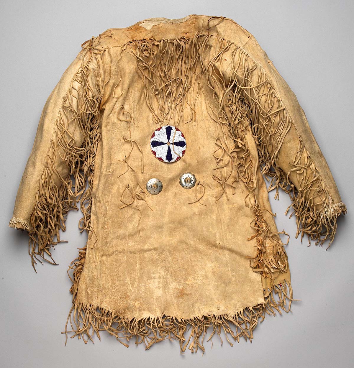 Mountain man's fringe leather jerkin shirt decorated with two nickel conchas and a large beaded rosette, undated. Gift of Richard W. Leche. NA.202.588