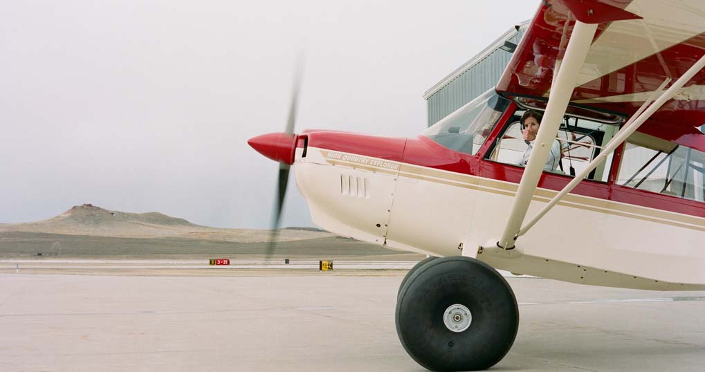 Lori Olson is the Director of the Upton Municipal Airport, a backcountry pilot, and a rural airstrip advocate. She is pictured here with "Papa Charlie," her American Champion 7GCGC high country plane. Photo by Lindsay Linton Buk.