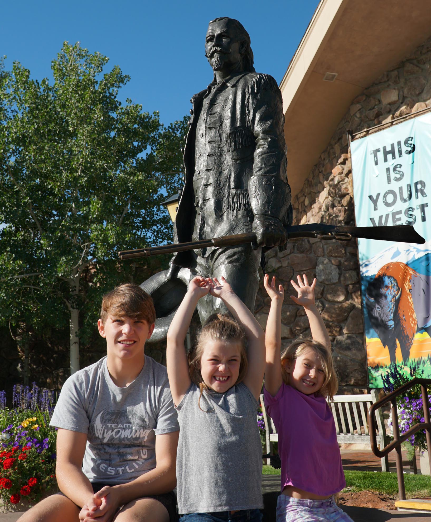 Three smiling children sitting in front of the Center of the West