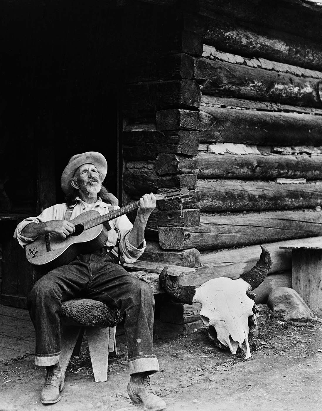 Jack 'Two Dog' Scott playing guitar on porch Pitchfork Ranch bunkhouse. MS 003 Charles Belden Collection. PN.67.62