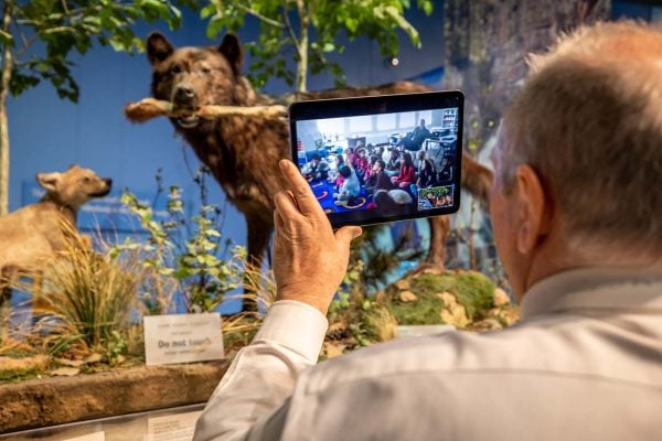 An educator holds up a tablet that shows the class he's speaking to for a Virtual Field Trip